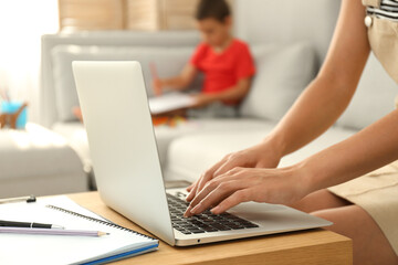 Young woman working on laptop while son drawing in living room, closeup. Home office concept