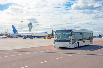 Bus for transporting passengers to boarding aircraft, against the background of a taxiing airliner on the apron of the airfield with a control tower. © aapsky