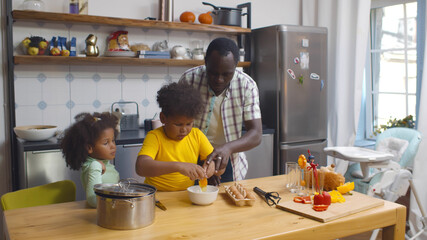 Happy african father with children cooking on paternity leave in kitchen
