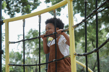 Active African little boy afro hair enjoy playing outdoors, 3 Years kid having fun climbing rope on...