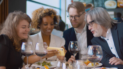 Mixed race people sitting at a table in restaurant using mobile phone