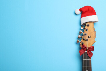 Top view of guitar with Santa hat and red bow on light blue background, space for text. Christmas...