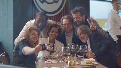 Happy diverse friends having dinner and taking selfie on smartphone at restaurant