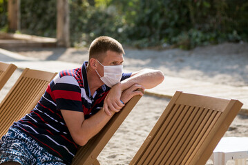 a man sits in a deckchair wearing a mask alone on the beach during the covid 19 flu epidemic