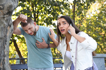 Woman calling ambulance to help man with heart attack in park