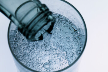 aus einer Glasflasche wird sprudelndes , klares Wasser in ein Glas geschenkt, Studioaufnahme