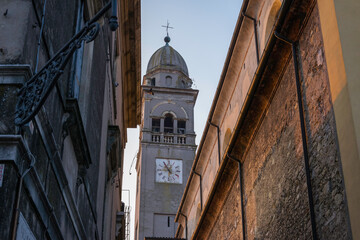 View of the bell tower of an ancient italian church in an alley during sunset