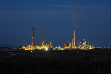 Pembroke oil refinery lit up at night with smoke rising from a chimney stack, Rhoscrowther on the Pembrokeshire coast, near Milford Haven, Wales, UK