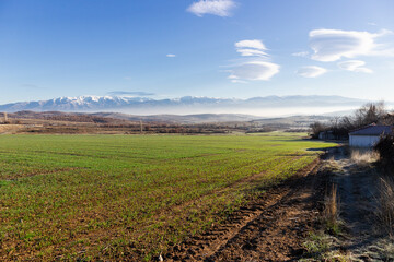 Landscape with a view of Rila mountain in Bulgaria. Green landfield and snowy mountains in the horizon. Landscape with a view of Rila mountain in Bulgaria.
