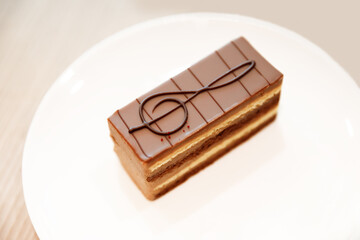 Brown chocolate cake decorated with the musical symbol treble clef on a white plate on the table. Selective focus.