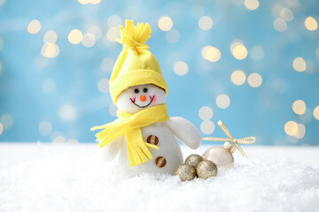 Snowman toy and Christmas balls on snow against blurred festive lights, closeup