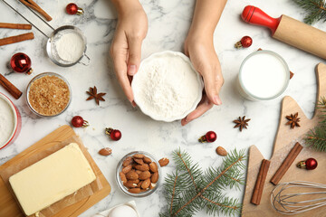 Woman cooking traditional Christmas cake at white marble table with ingredients, top view