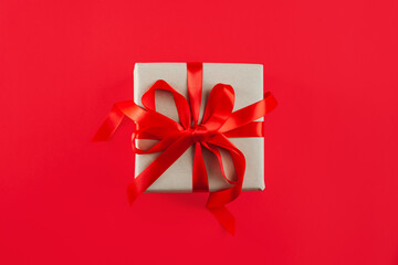 Gift box with a red ribbon and a bow isolated on the red background. Close-up. Top view.