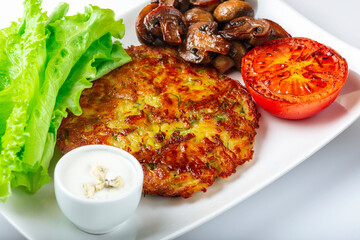 Potato pancakes with lettuce leaves, fried mushrooms, grill vegetables and blue cheese sauce. White background. Close up. Selective focus.