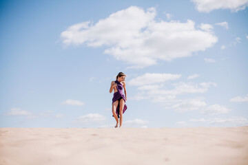 Fototapeta na wymiar A young, slender girl in a beige dress with purple cloth in her hands posing in the desert in the wind