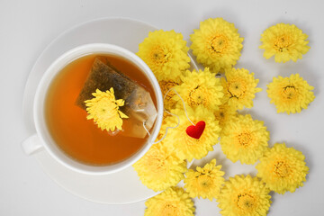 a cup of tea with a tea bag and yellow chrysanthemum. Flowers on a white saucer and light background
