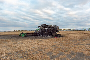 Back/Side View of Burnt Combine Harvester on Grain Field in Rural North Dakota, taken at Daytime with Cloudy Sky.