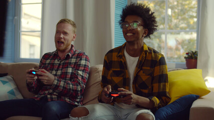 Smiling diverse male friends with gamepads playing video game at home