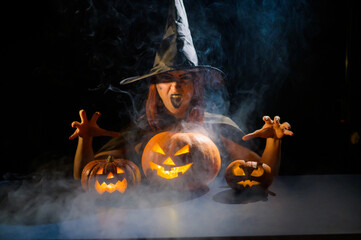The evil witch casts a spell on pumpkins. Portrait of a woman in a carnival halloween costume in...