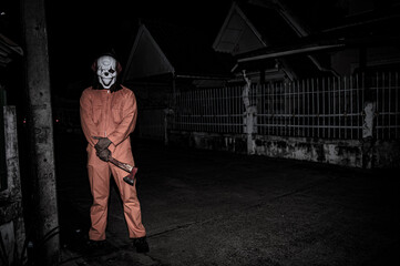 Fototapeta na wymiar Asian handsome man wear clown mask with weapon at the night scene,Halloween festival concept,Horror scary photo of a killer in orange cloth