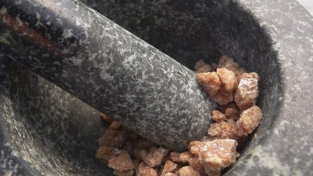 Large pieces of brown sugar are falling into the grey stone mortar in slow motion