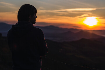 The silhouette of a young man in front of a sunset with the mountains in front of him