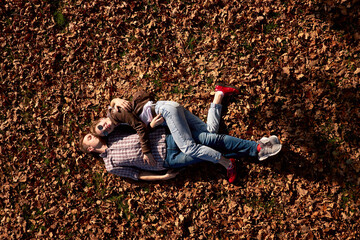Happy attractive funny young couple lying on the ground and hugging while walking in autumn park.