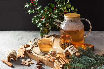 Glass teapot with blossoming tea and tea cup on grey table with Christmas gingerbread cookies.