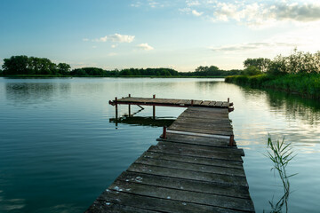 A wooden jetty on a calm lake and clouds on the sky