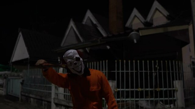 Asian handsome man wear clown mask with weapon at the night scene,Halloween festival concept,Horror scary photo of a killer in orange cloth	