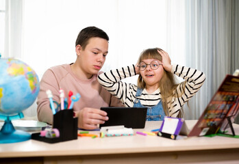 Obraz premium Emotions of two children at a Desk with a tablet. Study on the Internet. Home education, distance learning during quarantine