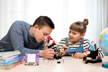 Children at home do biology lessons. The boy looks at the microscope. Home education, distance learning, home lessons