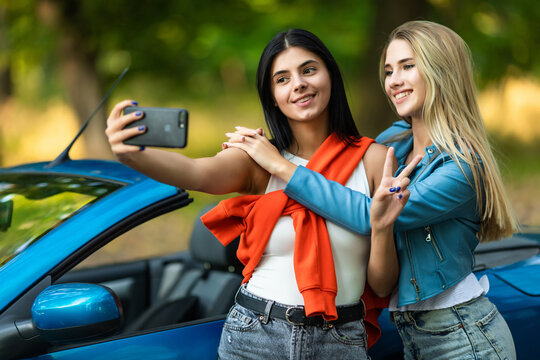Two attractive young women taking selfe in a convertible car on summer day