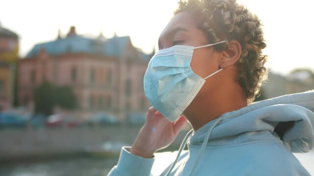 Side view of African young woman removing safety mask and breathing fresh air in city center