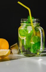 A vertical photo of a mug filled with water and ice cubes, sliced ​​lemon and mint leaves, next to a slices of lemon on a dark background