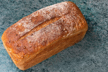 rectangular loaf of wheat bread with a baked shiny crust on the kitchen table.