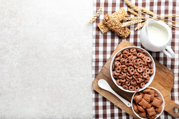 Chocolate corn flakes with milk in jar and granola bars on grey background