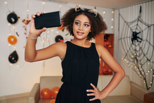 Smiling teenage girl filming herself in Halloween costume in decorated room