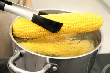 Taking boiled corn from pot with tongs in kitchen, closeup