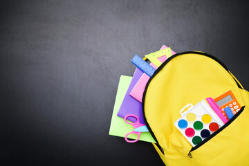Backpack with school supplies on black background