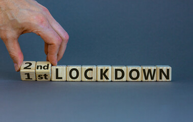 Symbol for a second lockdown. Hand turns cubes and changes the expression '1st lockdown' to '2nd lockdown'. Beautiful grey background. Medical and covid-19 pandemic concept, copy space.