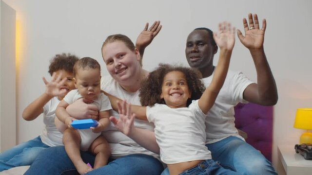 Family portrait of beautiful mixed race kids with multi-ethnic parents waving hands at camera
