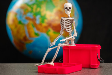 the skeleton sits on a box of red color, in the background the planet earth