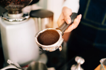 Close-up ground coffee bean in metal filter with handle holding by woman hand.Coffee making classes for entrepreneurs to start small businesses.