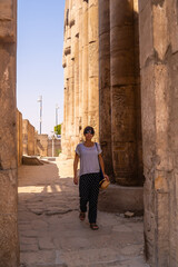 Fototapeta na wymiar A young tourist in a white t-shirt and hat visiting the temple and looking at the ancient egyptian drawings on the columns of the Luxor Temple, Egypt