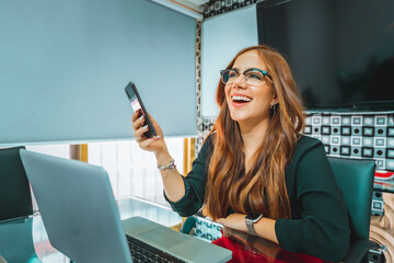 Mujer joven mexicana latina trabajando en oficina de empresa teléfono inteligente feliz alegre - obrazy, fototapety, plakaty