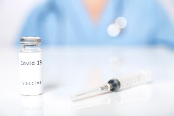 On the table lies a vaccine against the virus and a syringe in the background a doctor in blur.
