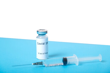 A syringe and a vial with a virus vaccine are on a blue table, top view.