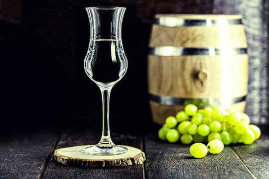 glass of Grappa on wooden background with old oak barrel, grape-based drink, distilled. Selective focus