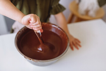 A little girl kneads chocolate dough for Christmas cookies with a large spoon.